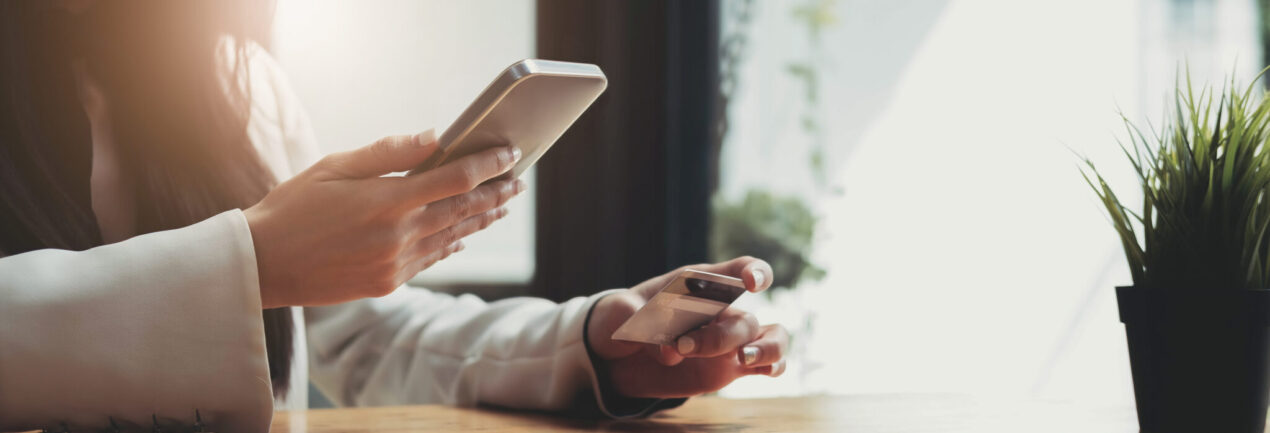 Hands holding business credit card and using mobile smart phone at cafe.